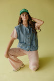 Woman wearing a denim vest and pink striped pants on a yellow background
