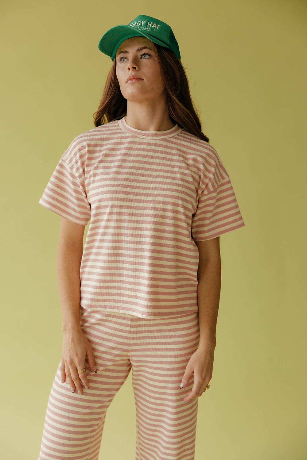 Person wearing a striped shirt and pants with a green cap against a yellow background