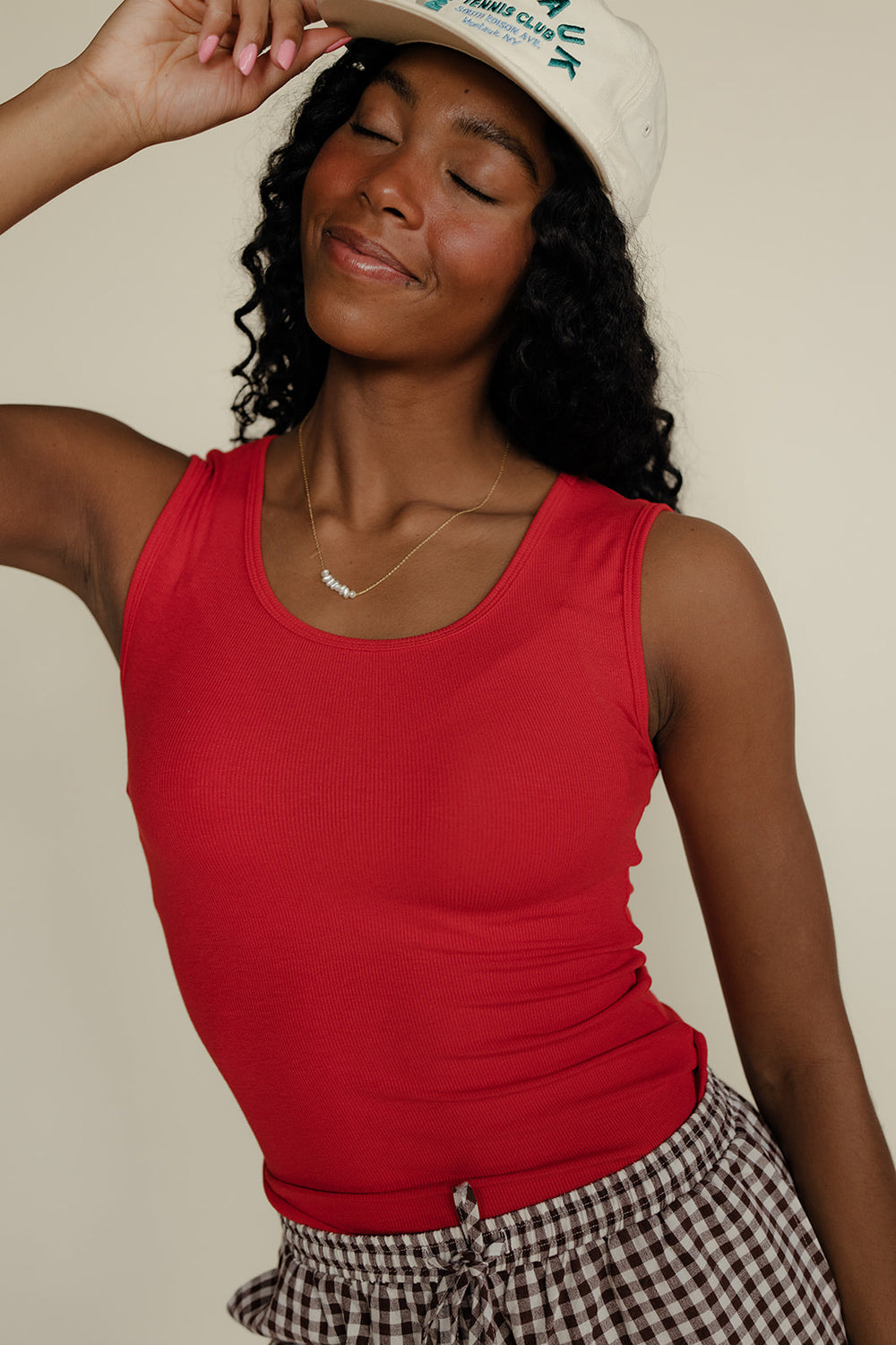 Woman wearing a red tank top and checkered skirt with a beige background