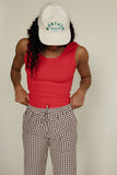 Person wearing a red tank top, checkered pants, and a white cap with 'Montana' text on a beige background
