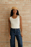 Woman wearing a white tank top and blue jeans against a brick wall