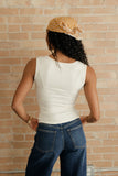 Person wearing a white sleeveless top and blue jeans with a yellow patterned headscarf against a brick wall.