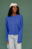 Woman wearing a blue cardigan and light-colored pants against a green background