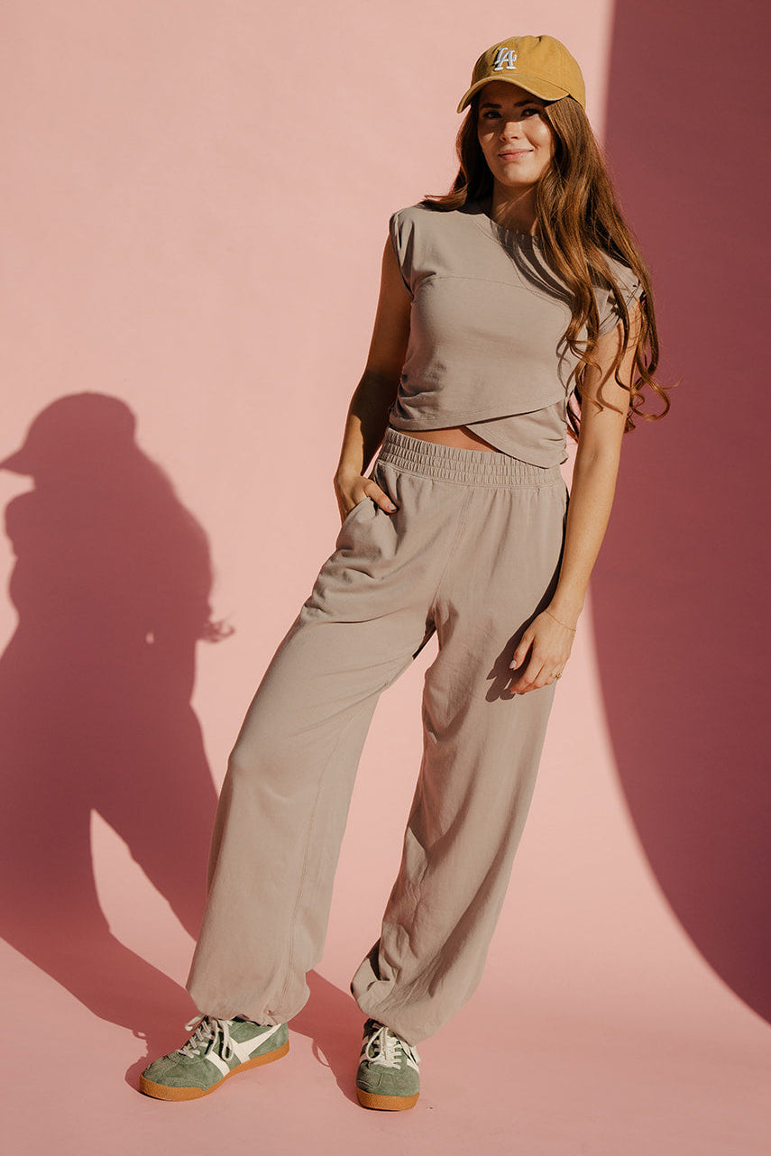 Woman wearing a beige outfit with a cap against a pink background