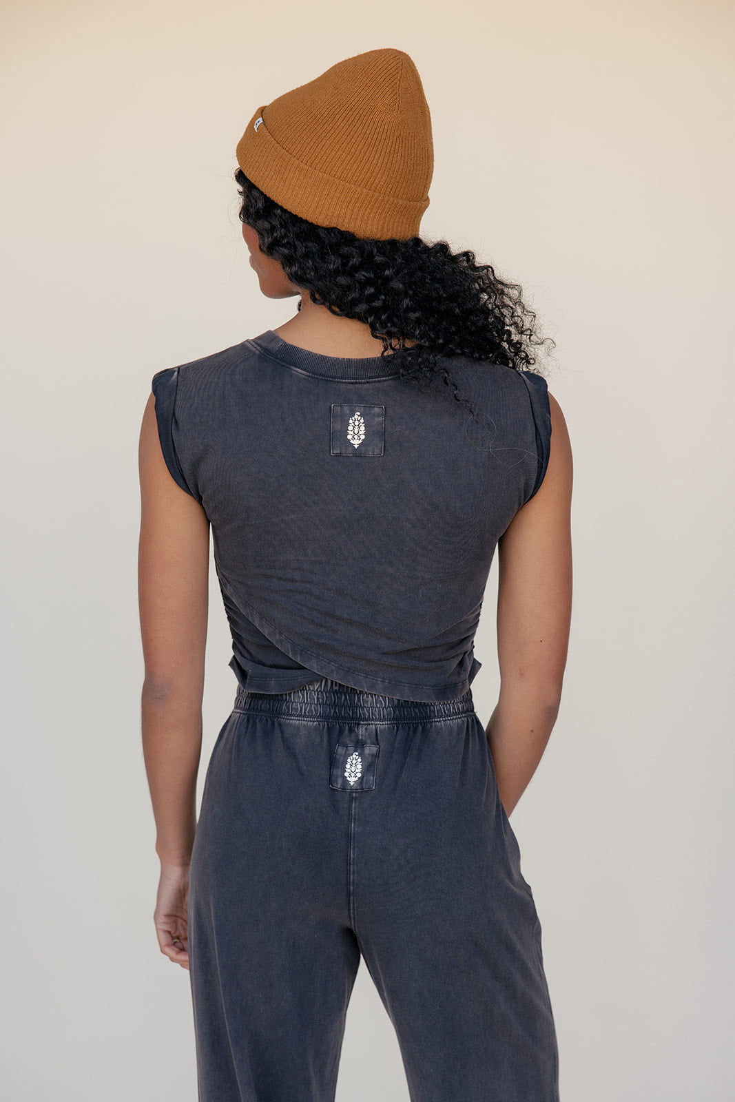 Person wearing a dark sleeveless top and jeans with a beige beanie on a plain background