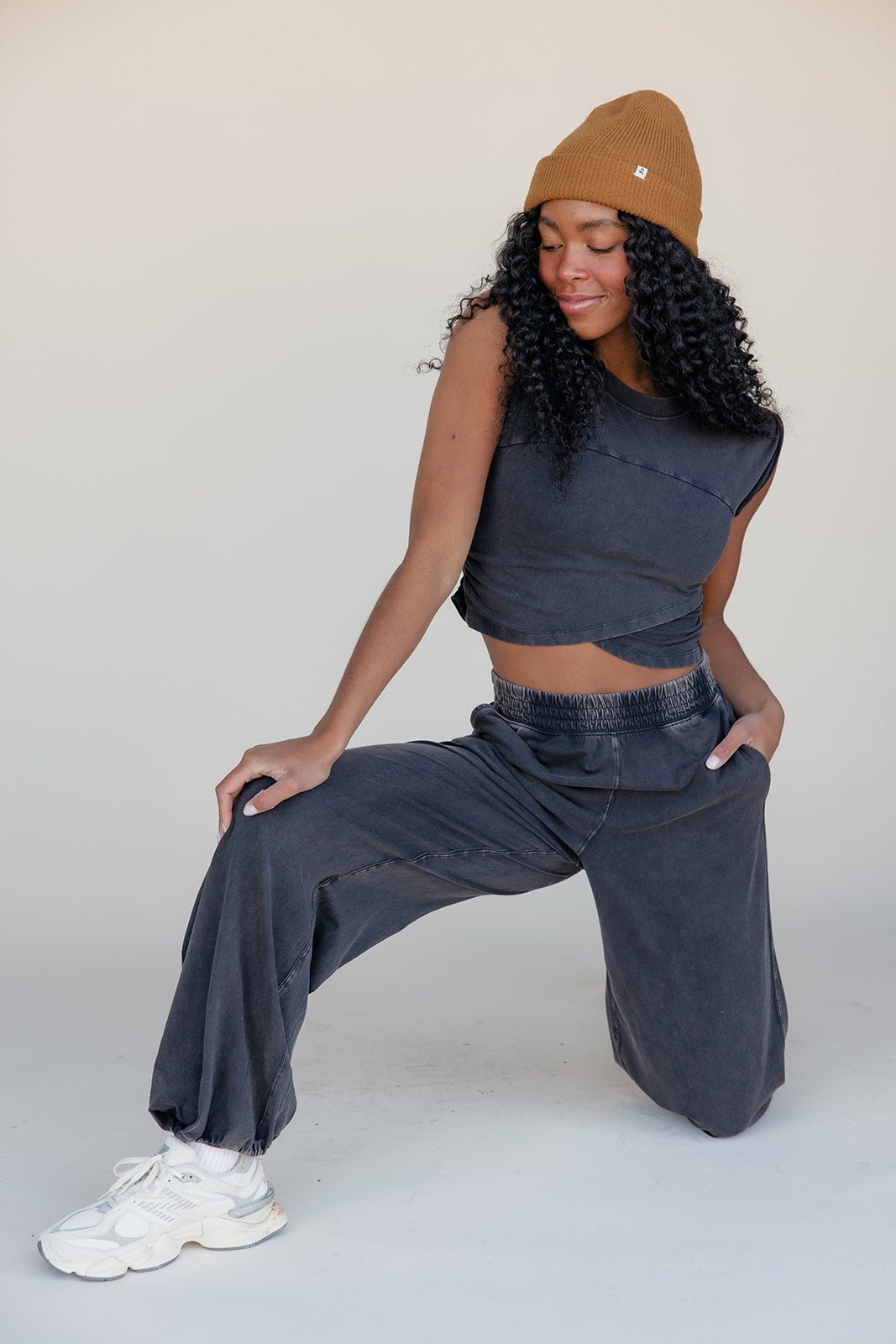 Woman wearing a sleeveless top and wide-leg pants with a beige beanie on a plain background