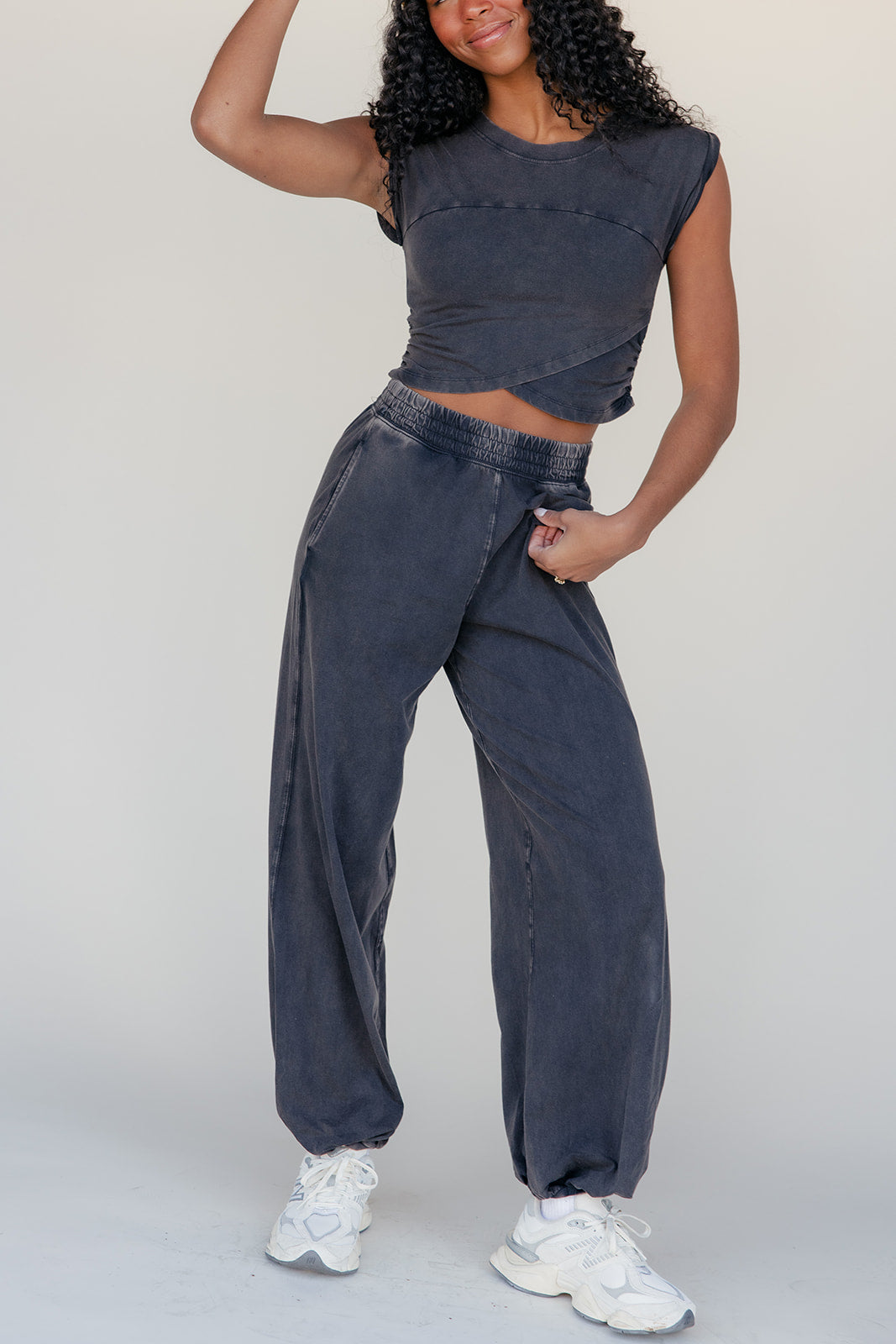 Person wearing a dark denim outfit with white sneakers on a plain background