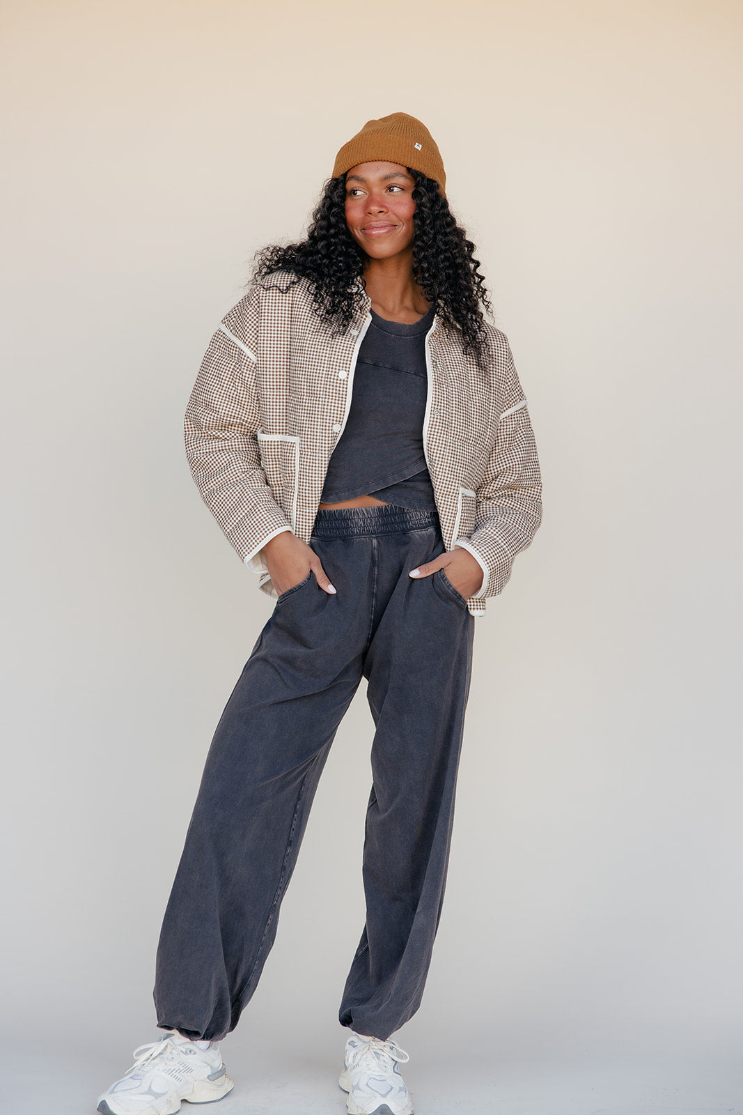 Person wearing a patterned jacket, dark pants, and a beanie against a plain background