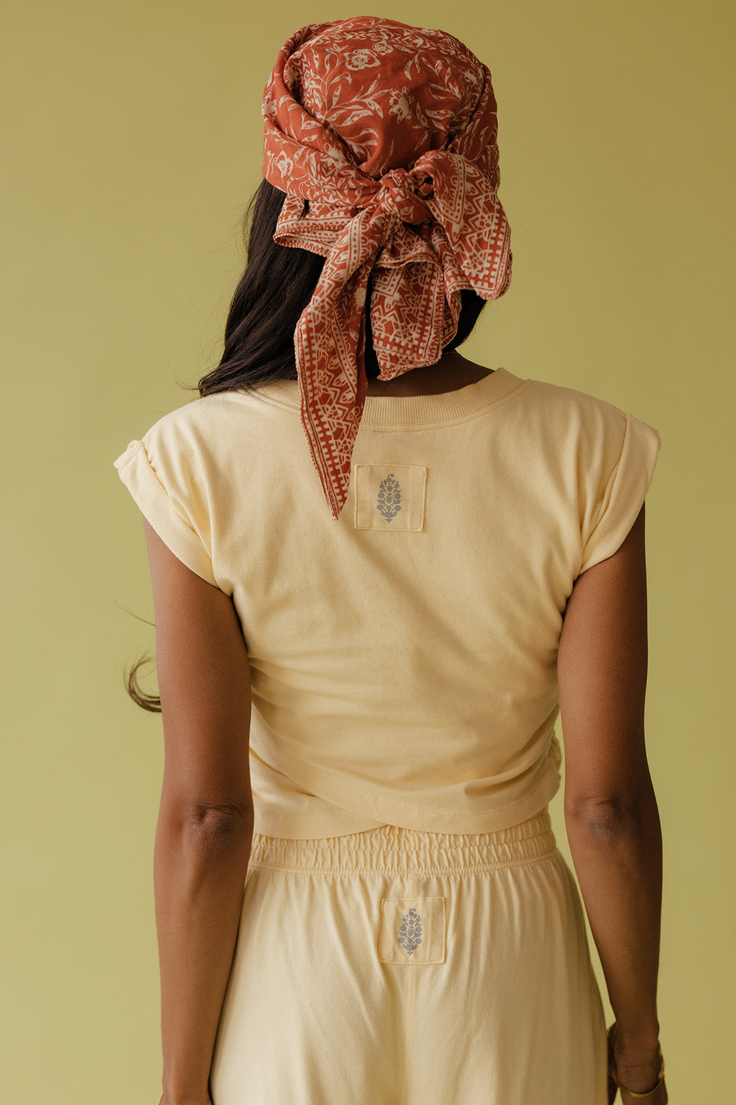 Person wearing a beige outfit with a patterned headscarf on a plain background
