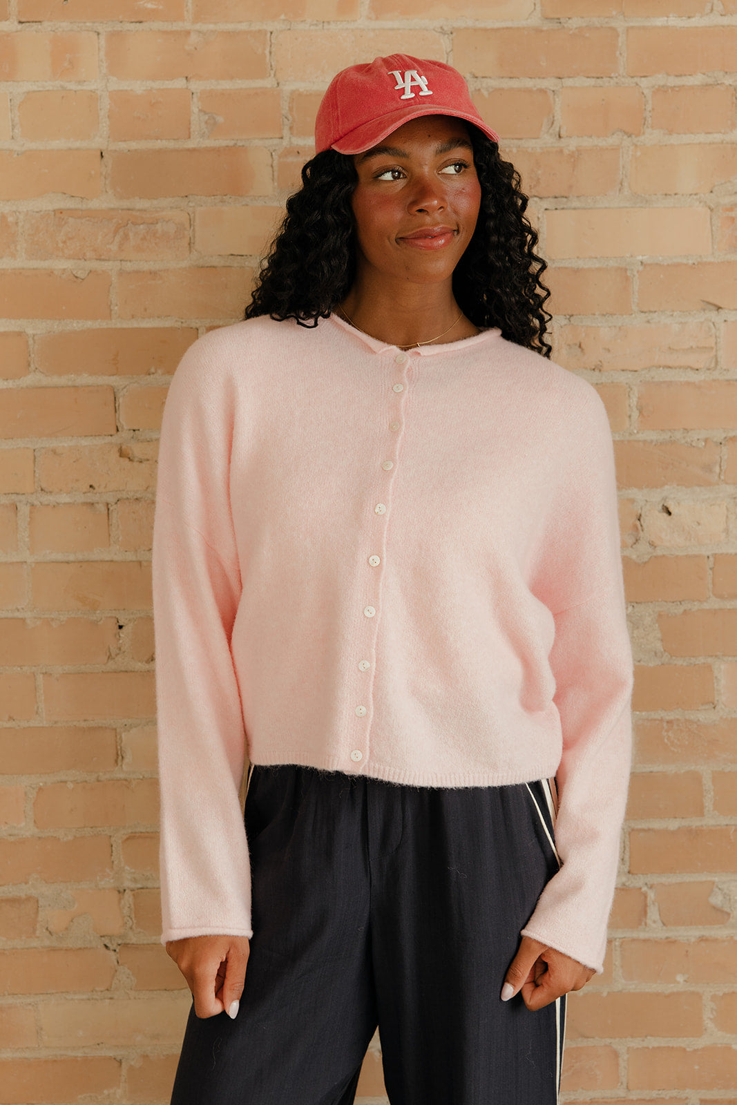 Person wearing a pink button-up shirt and red cap against a brick wall