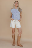 Woman wearing a light blue sleeveless shirt, white shorts, and brown boots on a beige background
