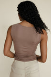 Person wearing a brown sleeveless top and beige pants against a plain background