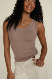 Woman wearing a brown tank top and white pants against a plain background