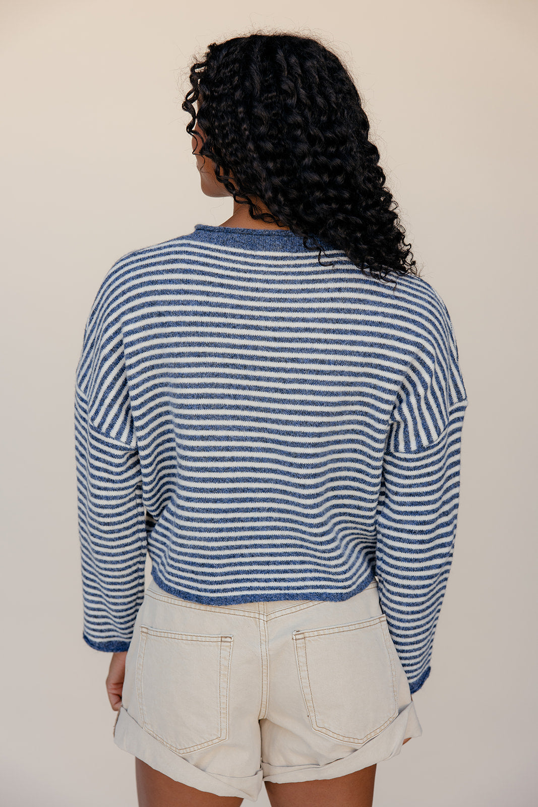 Person wearing a blue and white striped sweater and beige shorts against a plain background