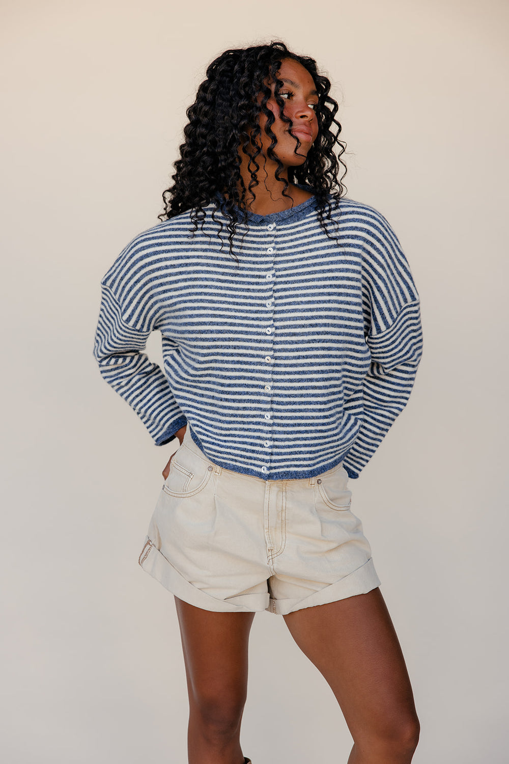 Person wearing a blue and white striped shirt and beige shorts against a plain background