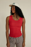 Woman wearing a red tank top and checkered pants with a white cap against a plain background