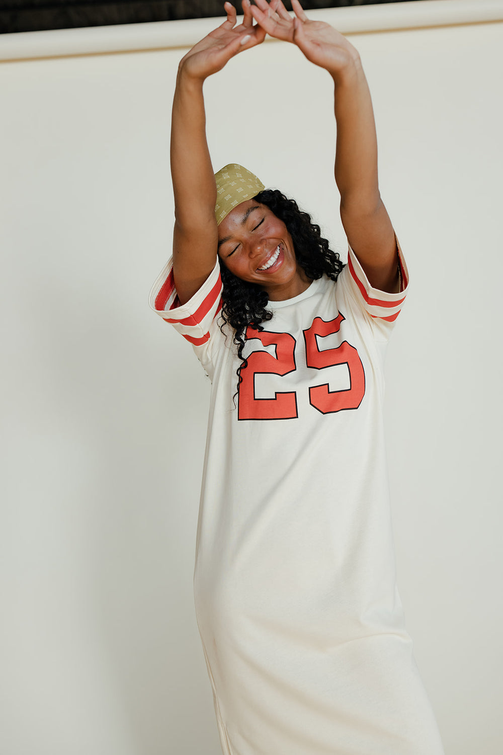 Woman wearing a white jersey with red numbers, smiling and stretching her arms above her head.