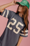 Person wearing a gray t-shirt with the number 25 and a green cap on a pink background