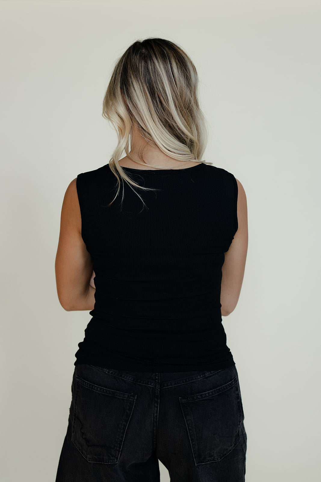 Person wearing a black sleeveless top and black pants against a plain background