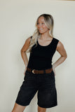 Woman wearing a black sleeveless top and black shorts with a brown belt against a plain background