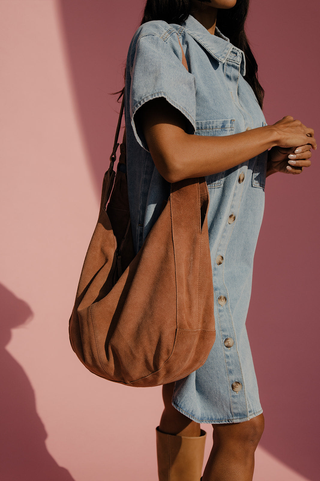 Person wearing a denim dress and brown bag against a pink background