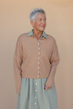 Woman wearing a brown cardigan over a green checkered shirt and skirt against a beige background