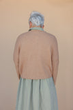 Person wearing a beige sweater and green checkered skirt against a beige background