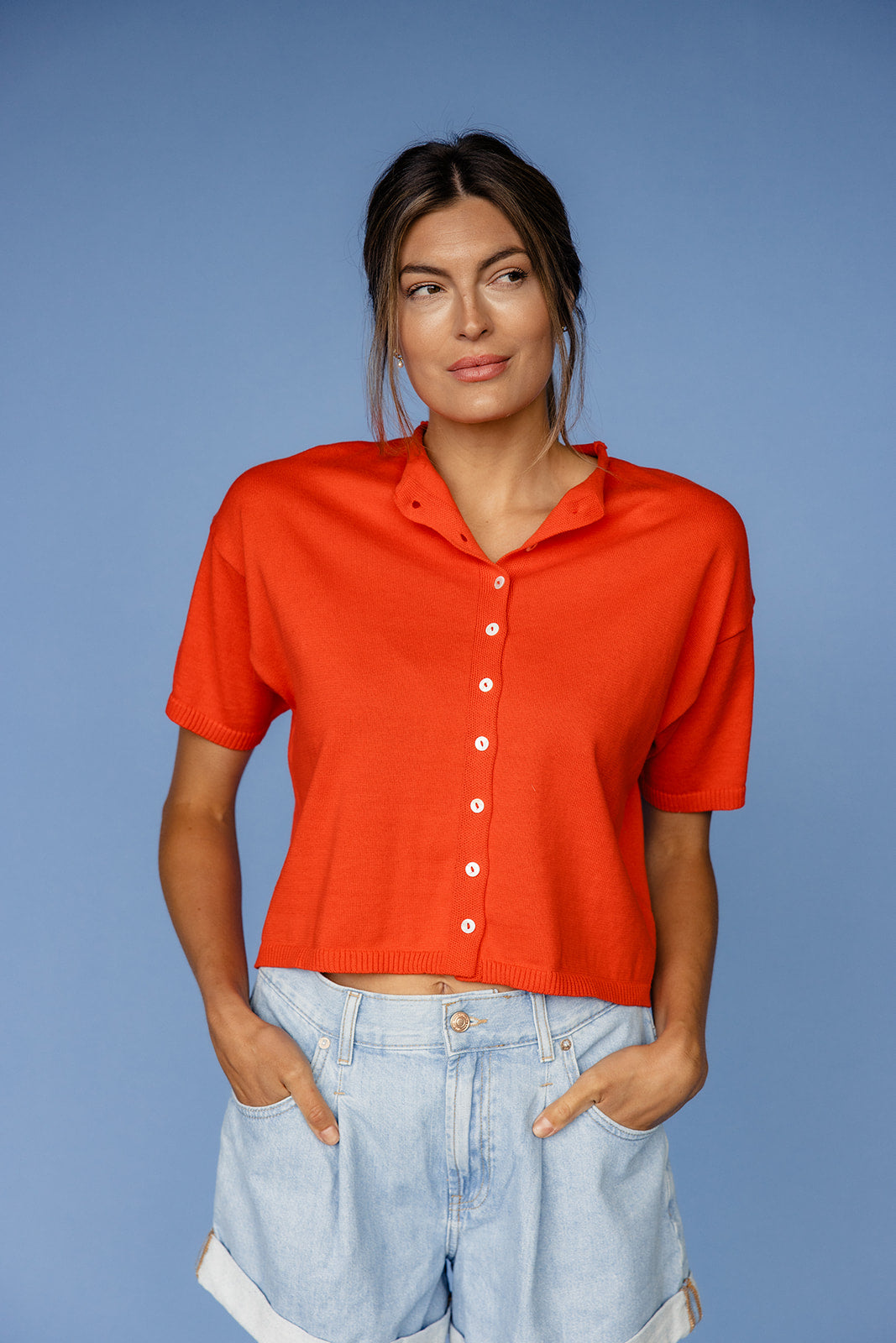 Woman wearing a red shirt and light blue jeans against a blue background