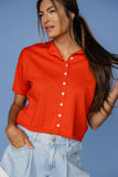 Woman wearing a red short-sleeve shirt and light blue jeans against a blue background
