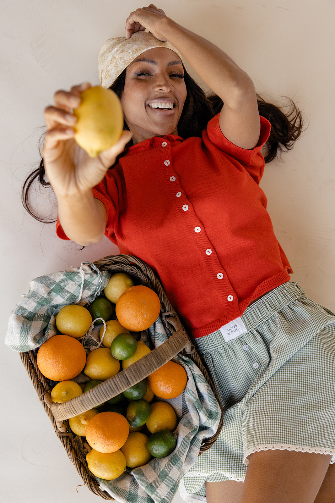 Woman holding a lemon with a basket of fruits on a checkered cloth