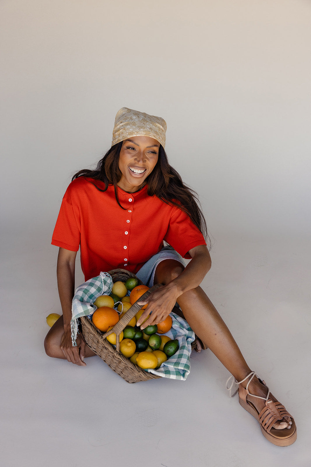 Woman in red shirt and beige hat holding a basket of fruits on a white background
