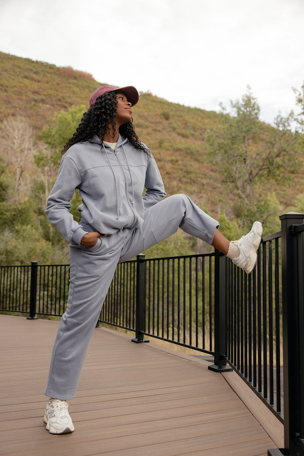 Person in gray tracksuit standing on a wooden deck with a scenic background